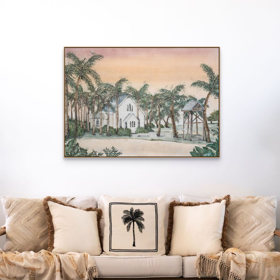 Far Northern Skies print above a beige sofa with palm tree pillows and a white church-themed cushion.