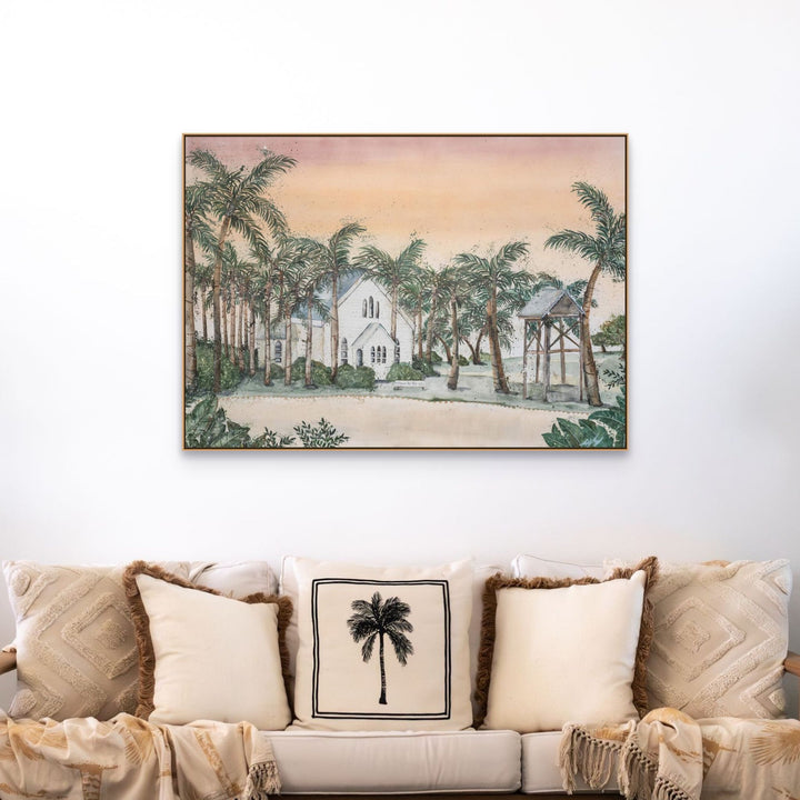 Far Northern Skies print above a beige sofa with palm tree pillows and a white church-themed cushion.
