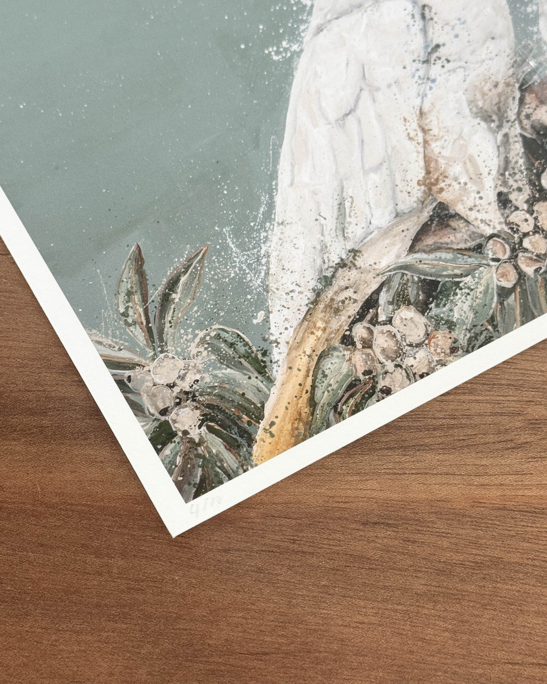 Corner of a fine art print resting on a timber surface, showing a white cockatoo&
