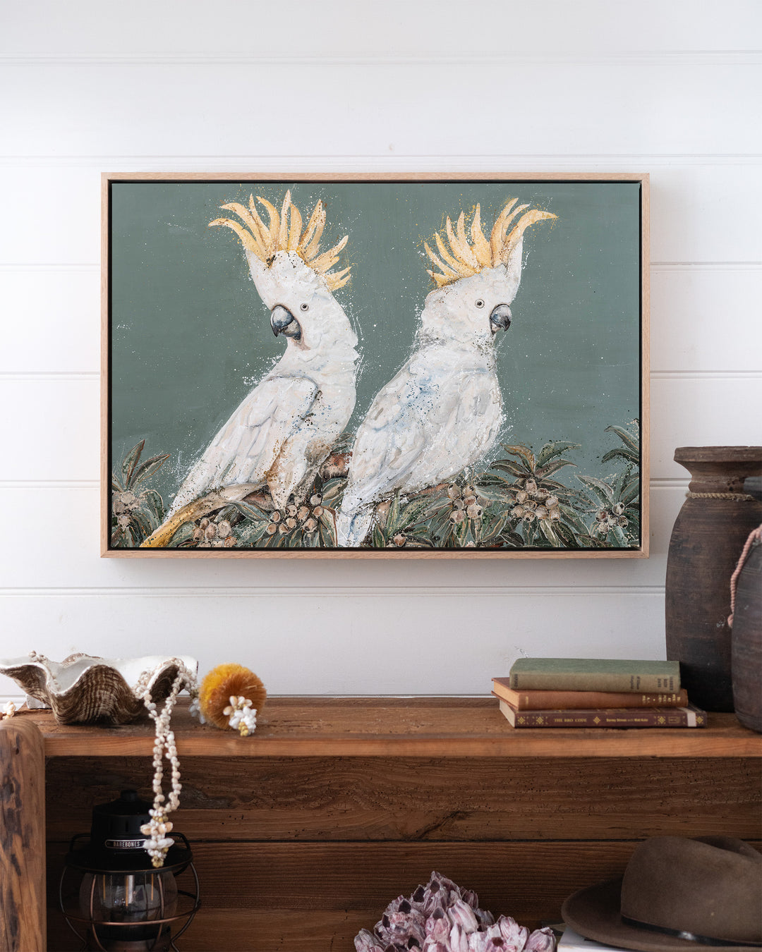 Feathers and Mayhem white cockatoo fine art print by Stephanie Elizabeth, framed canvas in an oak frame above a bookshelf