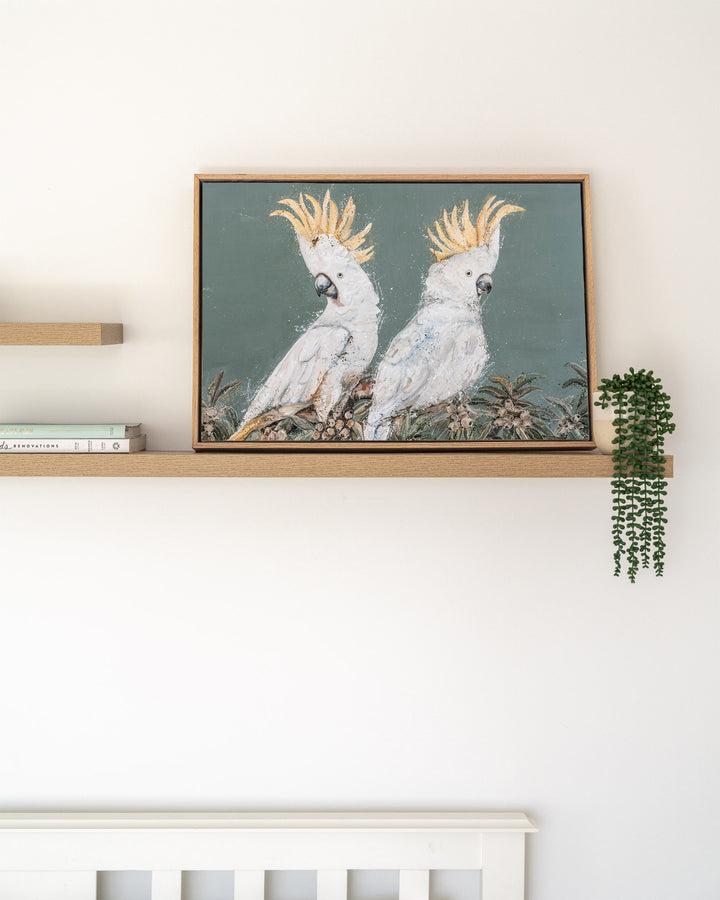 Feathers and Mayhem white cockatoo fine art print by Stephanie Elizabeth, framed canvas in an oak frame on a shelf