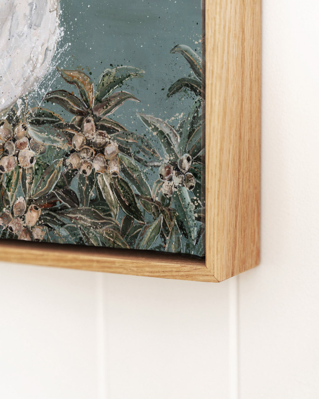 Close-up detail of "Feathers and Mayhem" white cockatoo canvas by Stephanie Elizabeth, showing thick paint texture on gum leaves and nuts, framed in natural oak.