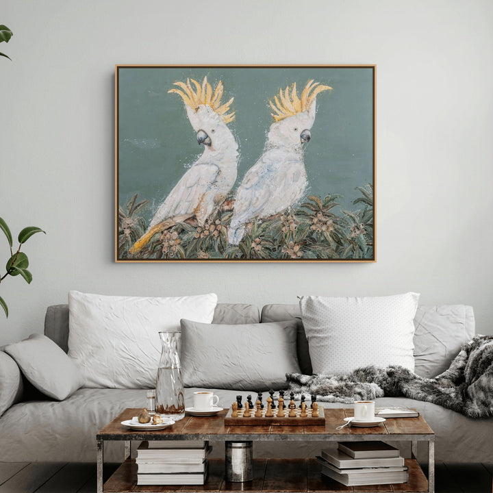 Gray couch with cushions and coffee table in a living room, featuring Feathers and Mayhem artwork on the wall.