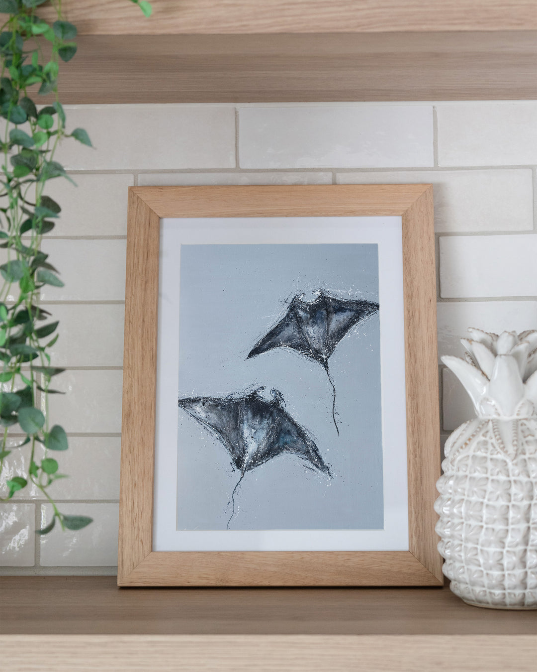 Heart Beats Slow manta rays fine art print by Stephanie Elizabeth, framed paper print in an oak frame on a kitchen shelf