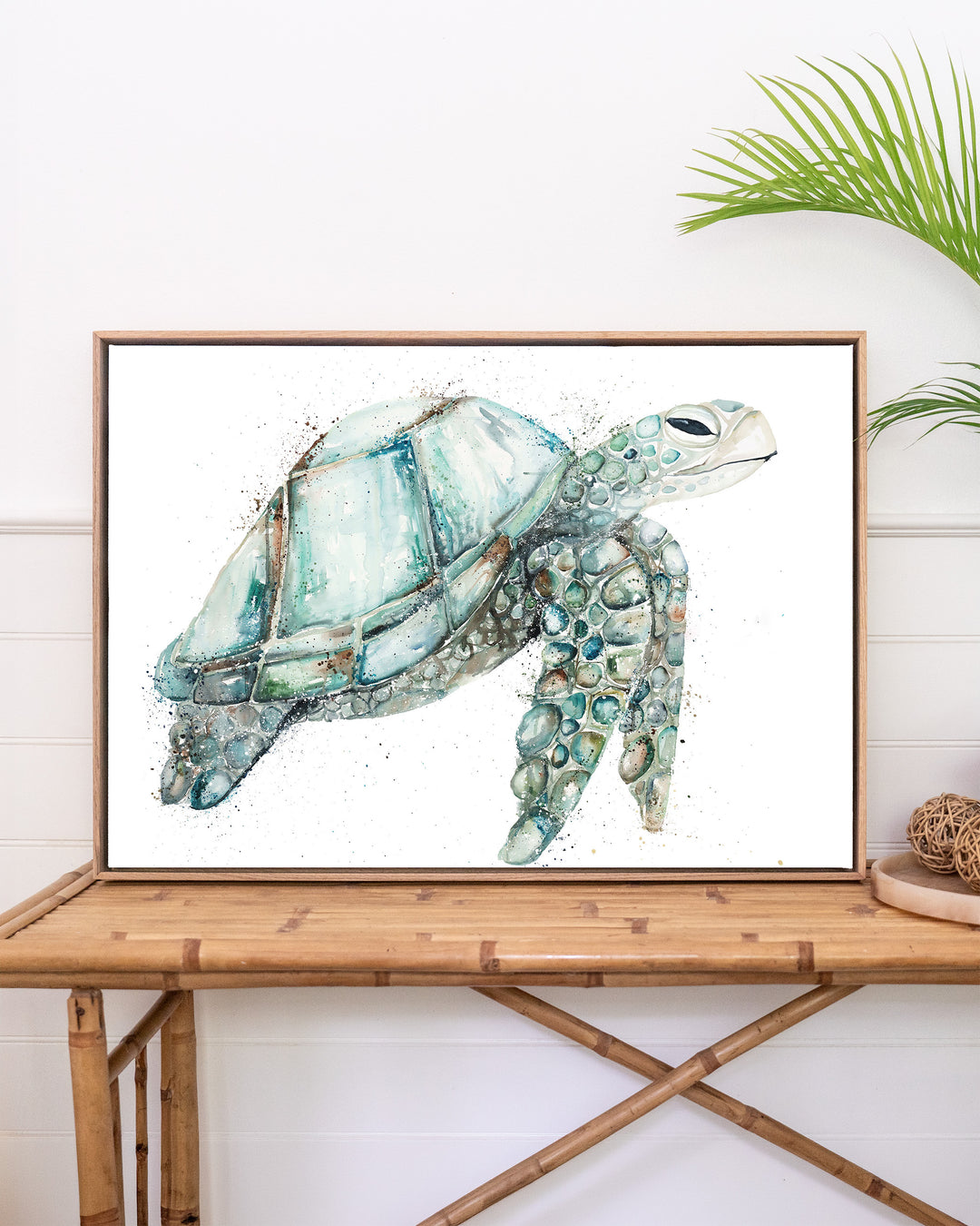 Jade sea turtle fine art print by Stephanie Elizabeth, framed canvas in an oak frame above a rattan table