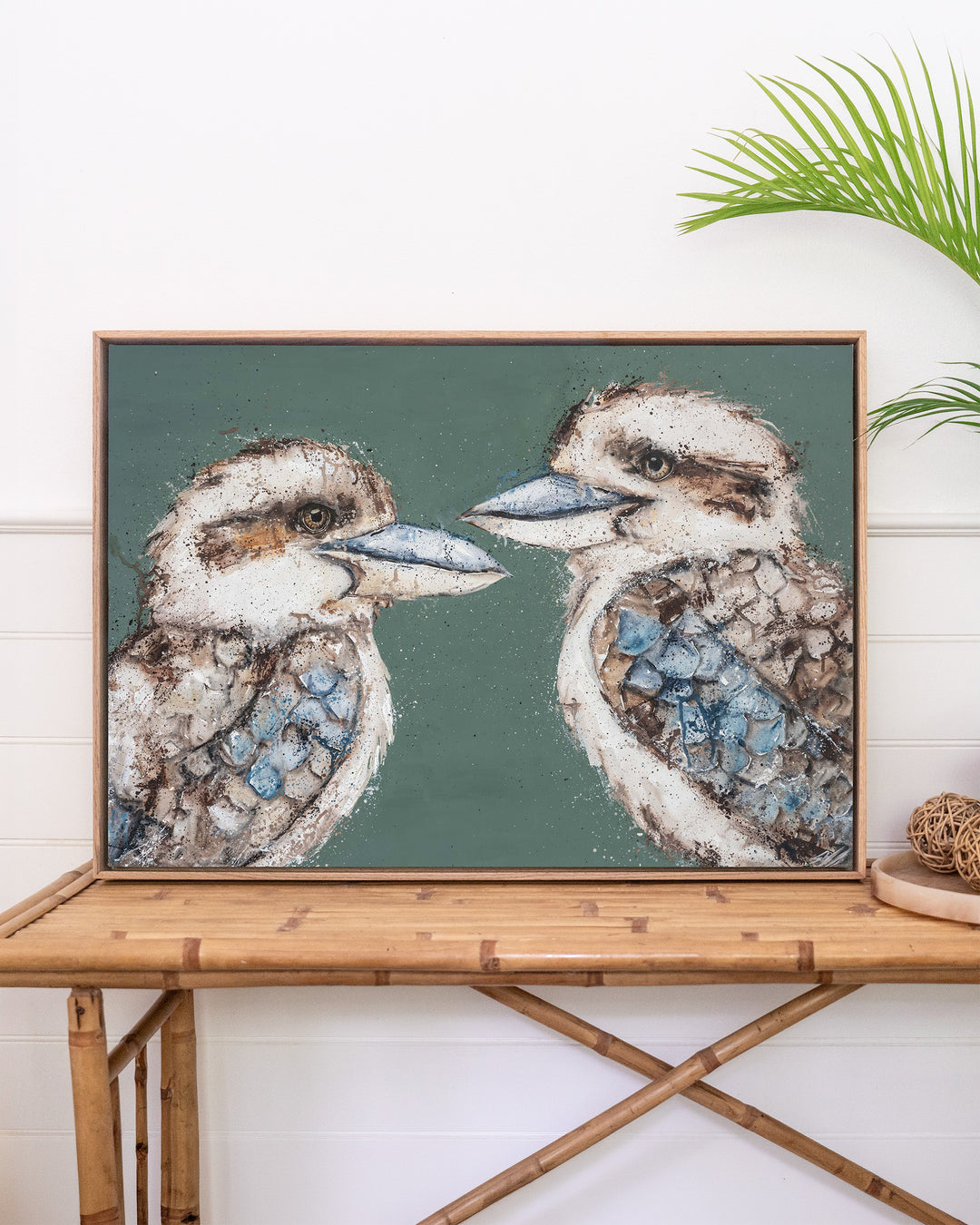 Love Me Now – kookaburras, framed canvas in oak float frame, styled on a rattan table