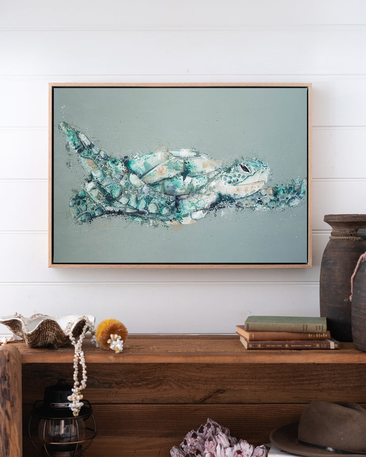 Message in a Bottle green sea turtle fine art print by Stephanie Elizabeth, framed canvas in an oak frame above a bookshelf