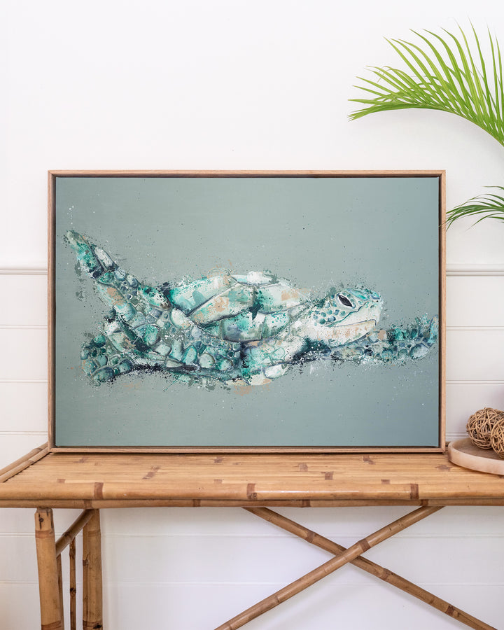 Message in a Bottle green sea turtle fine art print by Stephanie Elizabeth, framed canvas in an oak frame above a rattan table