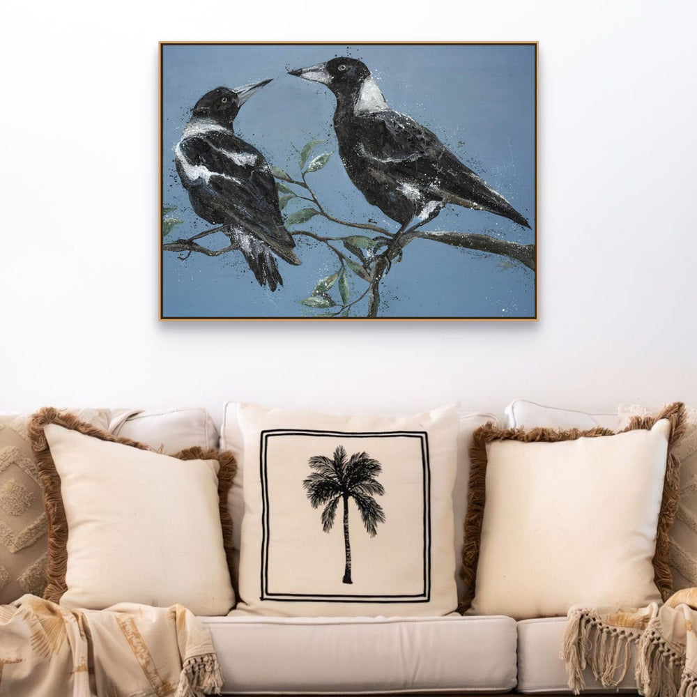 Monochrome Muses Magpie fine art print hangs above a beige sofa with palm-patterned cushions.