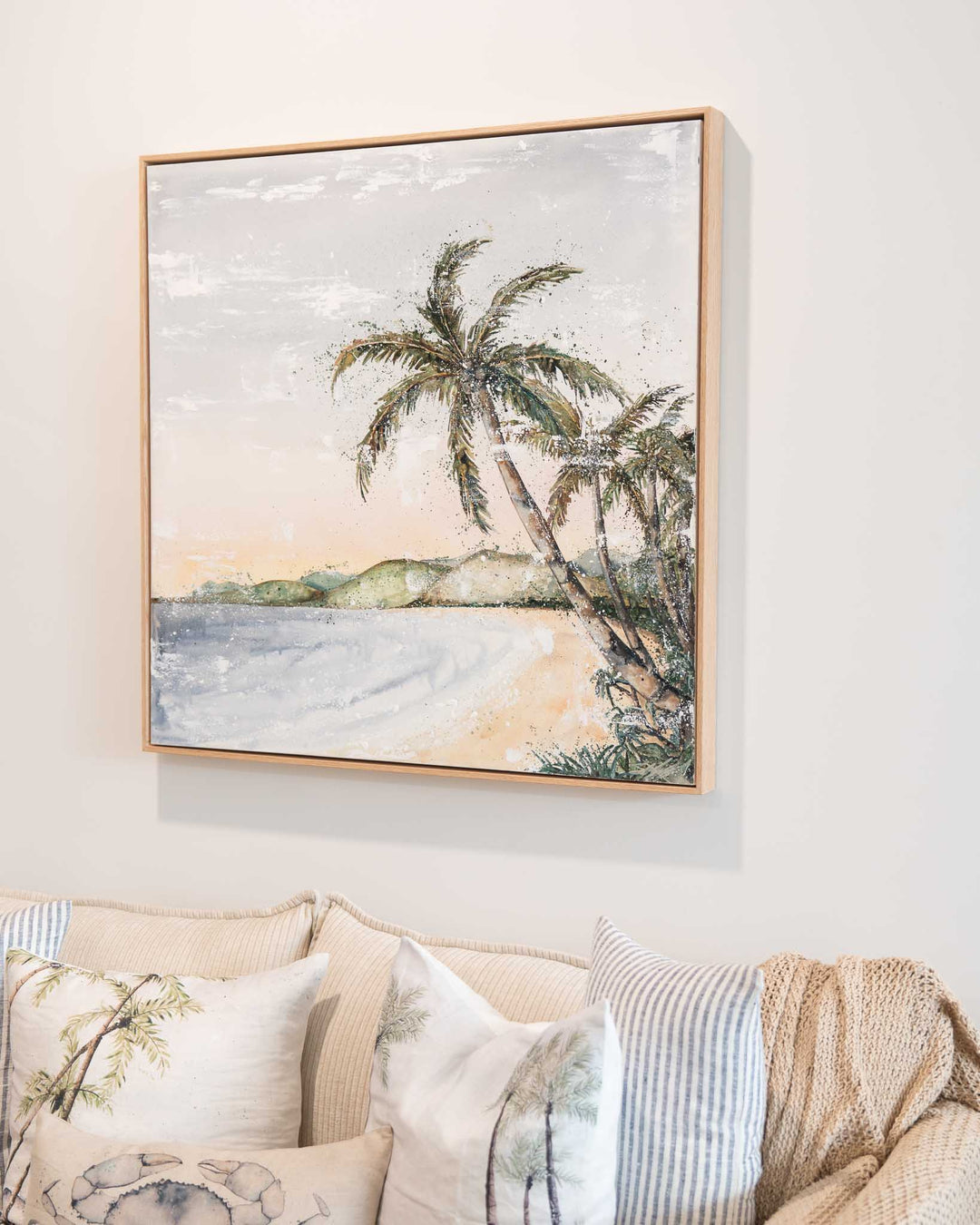 Morning Ritual“ artwork hangs above a beige couch decorated with pillows and a knit throw.