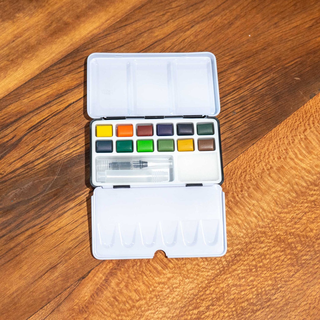 SEA Gallery Nature Watercolour Pocket Set with 12 bright colors, a brush, and mixing trays displayed on wood.