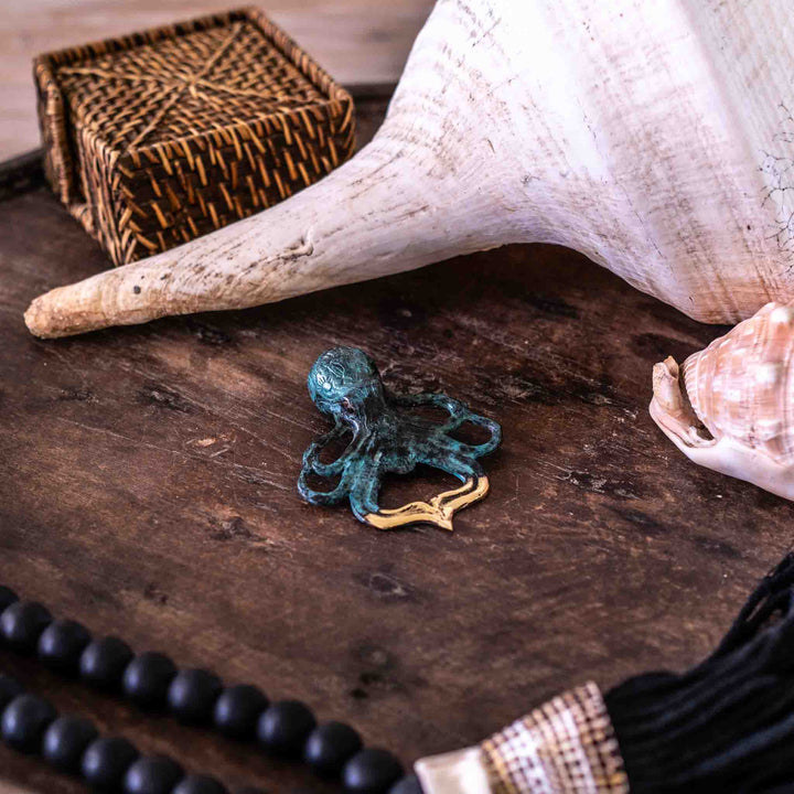 Octopus Bottle Opener in aged brass displayed on a tray with seashells and black beads for coastal decor.