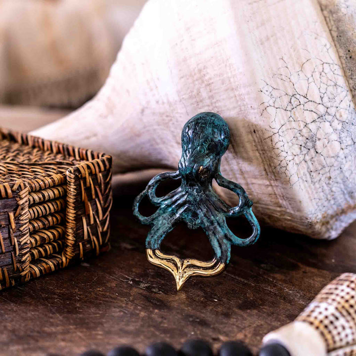 SEA Gallery Octopus Bottle Opener in aged brass placed on a table next to a wicker box and a seashell.