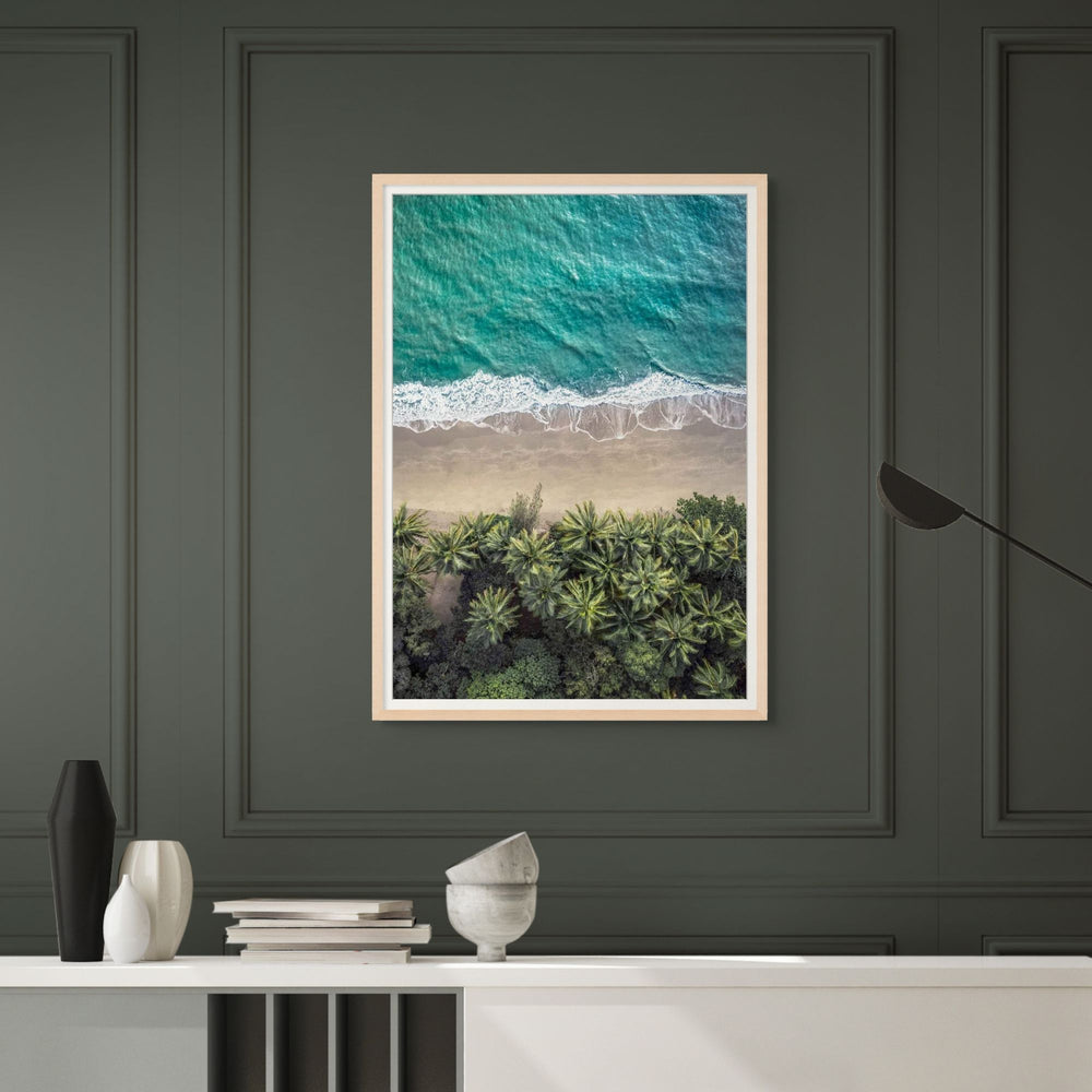 Framed artwork of a beach scene with palm trees on a dark green wall.