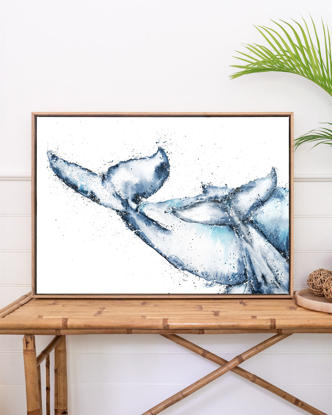 One Tale, Two Tails – whale tails, framed canvas in oak float frame, styled on a rattan table