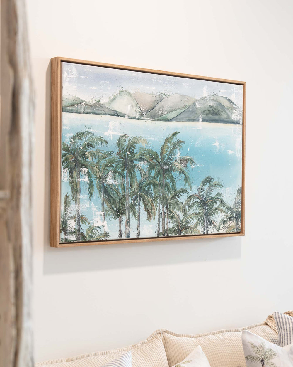 Over Flagstaff by Stephanie Elizabeth above a beige sofa, showing palms, water, and distant mountains for a tranquil feel.
