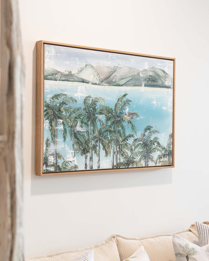 Over Flagstaff by Stephanie Elizabeth above a beige sofa, showing palms, water, and distant mountains for a tranquil feel.