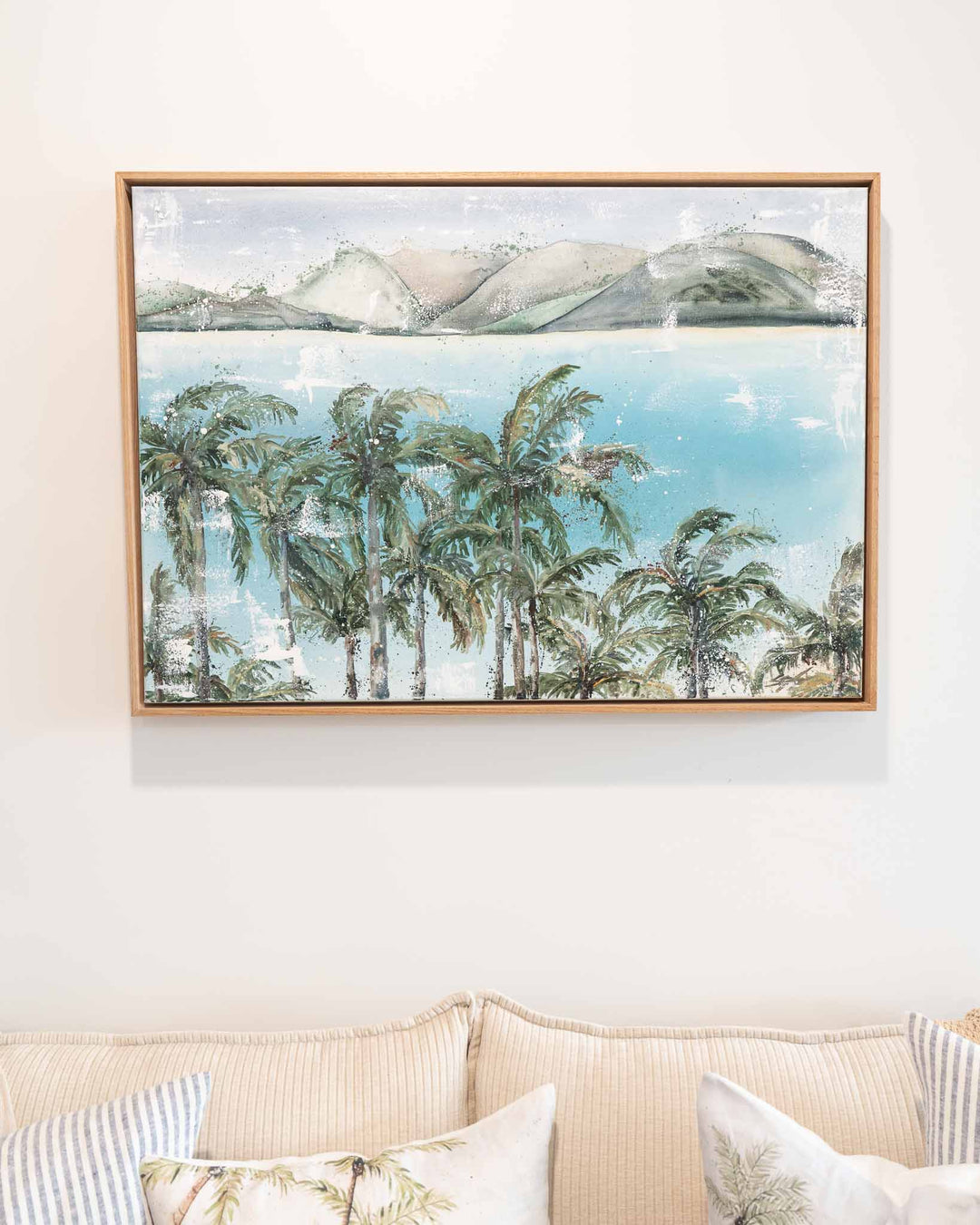 Over Flagstaff“ by Stephanie Elizabeth: tranquil palms, water, and mountains above a beige couch.