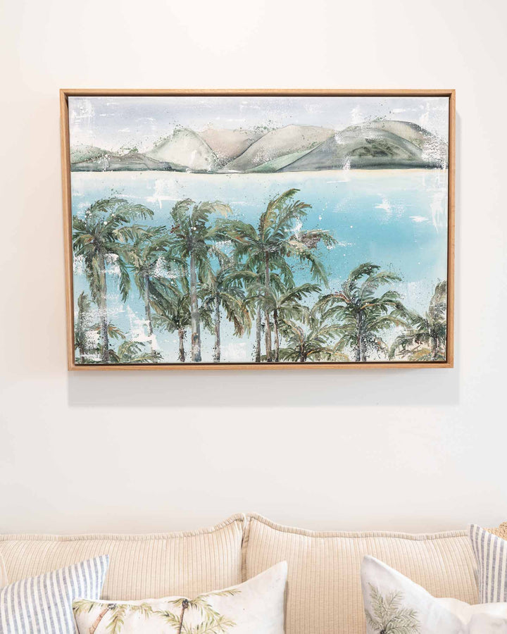 Over Flagstaff“ by Stephanie Elizabeth: tranquil palms, water, and mountains above a beige couch.