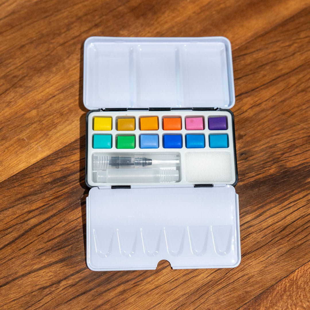 SEA Gallery Pastel Watercolour Pocket Set with 12 soft paints, water brush, and tray displayed on a wooden surface.