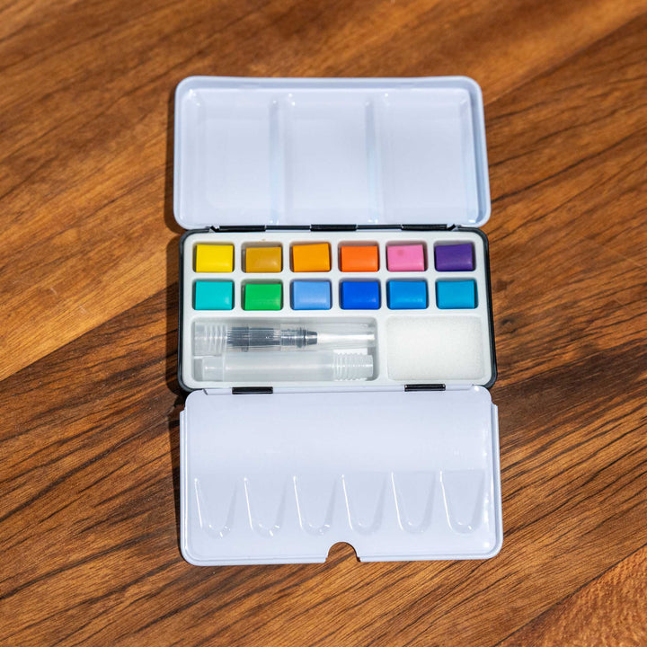 SEA Gallery Pastel Watercolour Pocket Set with 12 soft paints, water brush, and tray displayed on a wooden surface.