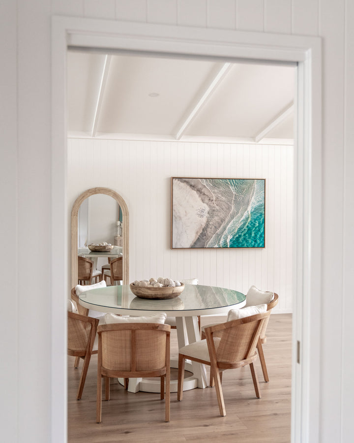 Bright dining room with a round table, six chairs, and Pearls and Pelicans wall art on the wall.