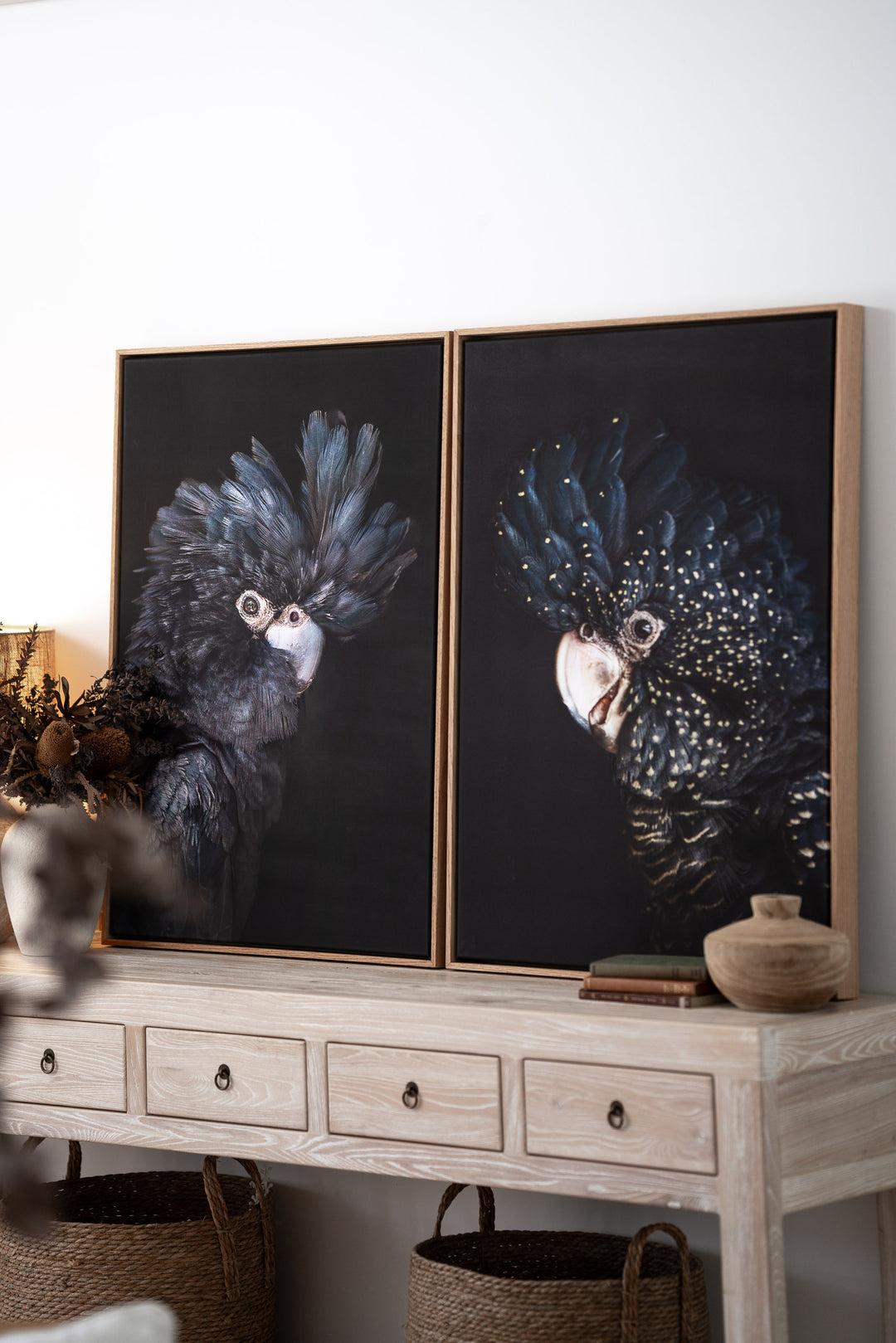 “A Little More Action” black cockatoo prints on a light wood console with storage baskets underneath.