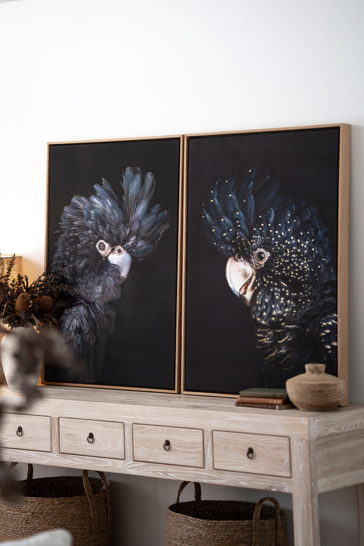 “A Little More Action” black cockatoo prints on a light wood console with storage baskets underneath.