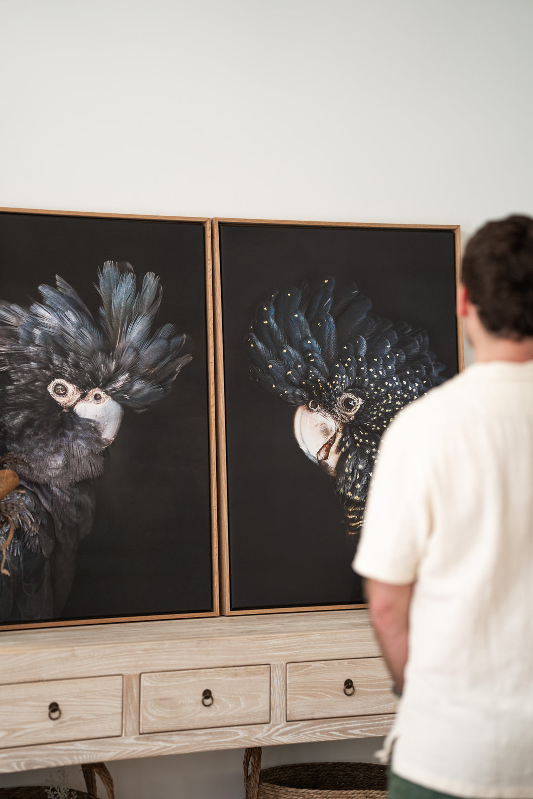 Two “A Little Less Conversation | Black Cockatoo” prints displayed on a console table with someone looking at them.