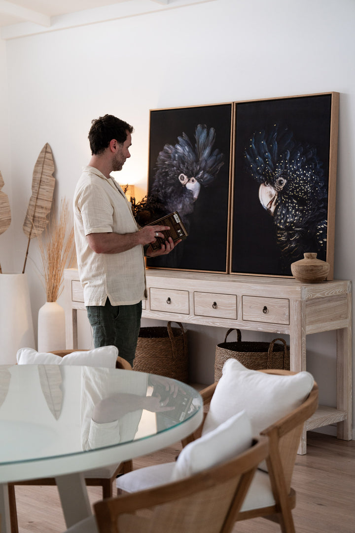 A man looks at “A Little More Action | Black Cockatoo” artwork in a modern living room setting.
