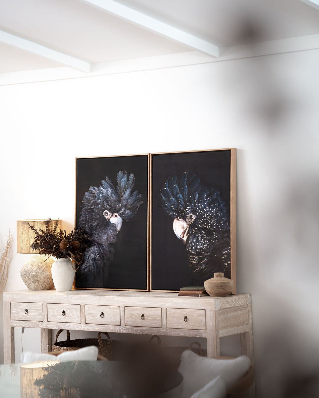 A Little More Action | Black Cockatoo artwork displayed on a light wood console with vases and bowls in sunlight.