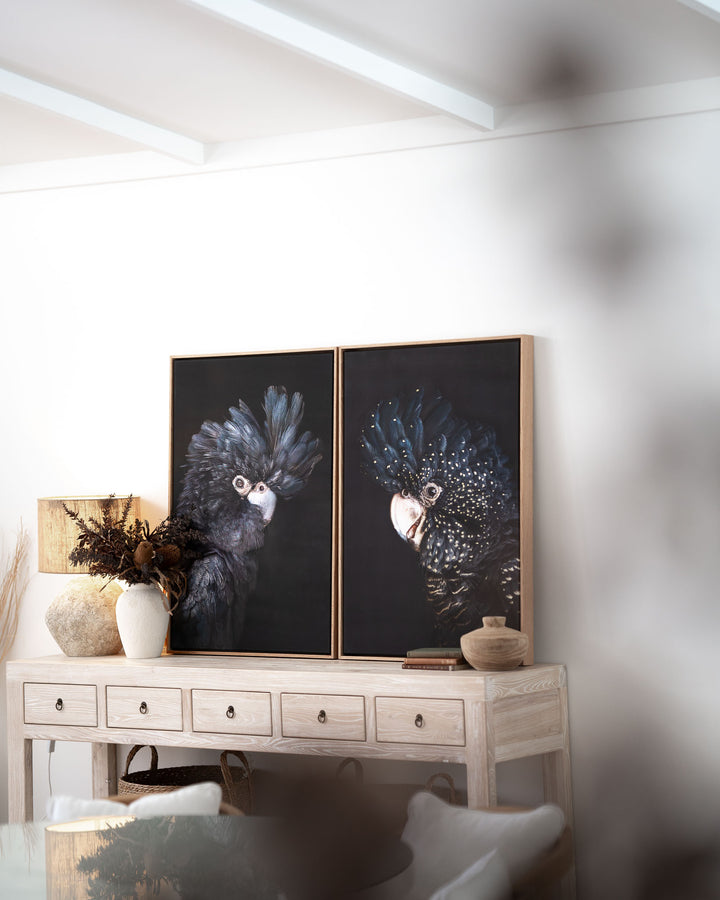 A Little More Action | Black Cockatoo artwork displayed on a light wood console with vases and bowls in sunlight.
