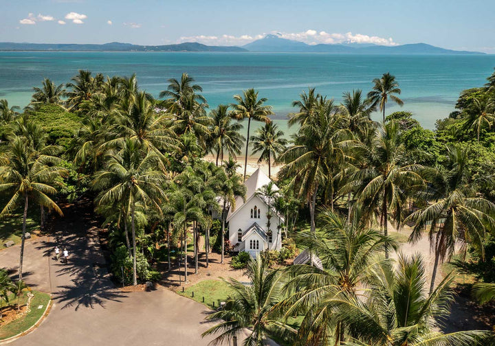 Rolling to the Seaside – Aerial view over St Mary’s, Port Douglas on a perfectly flat day with tropical waters, blue skies, and distant mountains | Unframed Rolled Print
