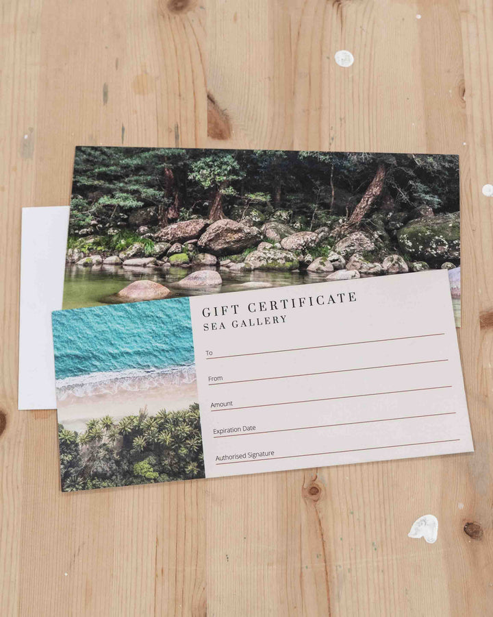 SEA Gallery Gift Card with a beach and forest design displayed on wood inside the Port Douglas gallery.