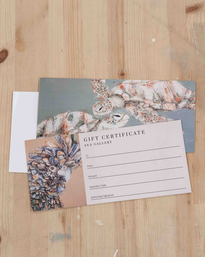 SEA Gallery Gift Card featuring sea turtle and pinecone artwork on a wooden surface.
