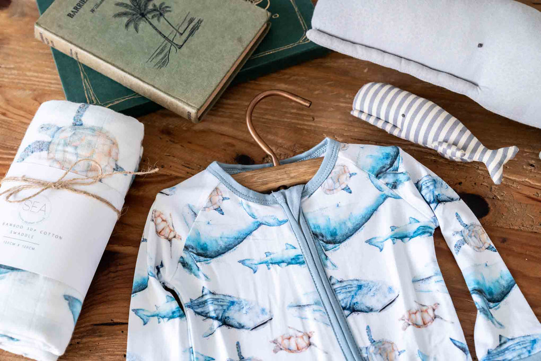 Baby onsie romper with swaddle surrounded by books and whale toys
