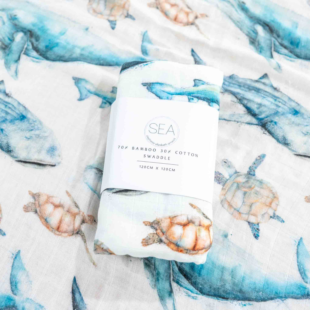 Bamboo swaddle blanket with sea-themed design featuring sharks, turtles, and fish on a white background.