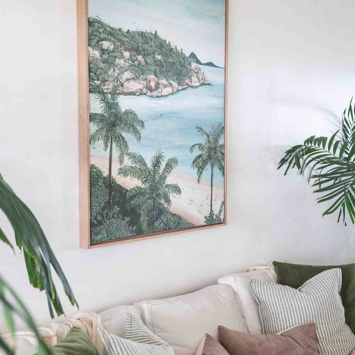 She Calls Me Back – framed coastal painting of Port Douglas shoreline with palm trees and rocky headland displayed in relaxed interior setting | Original Artwork