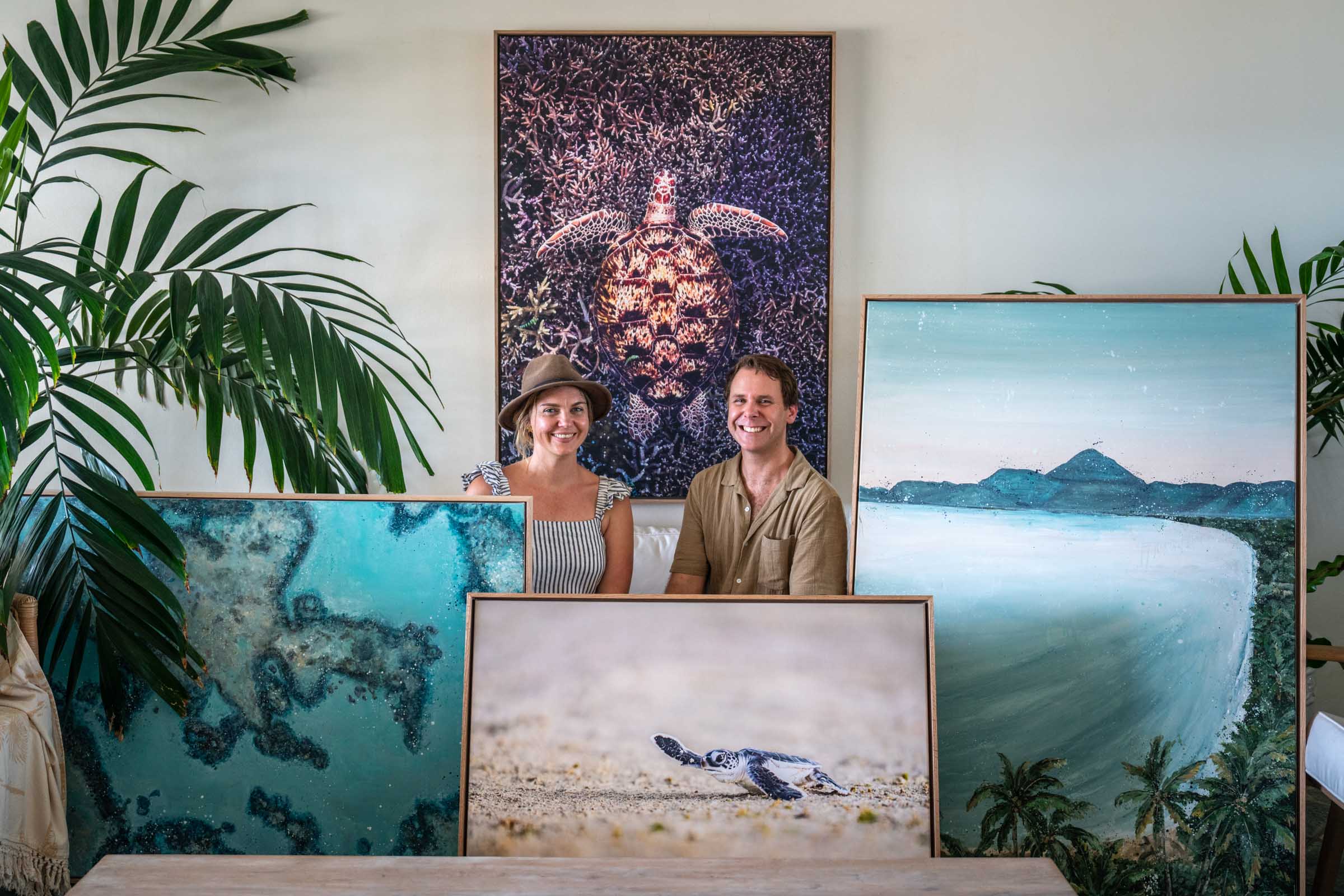 Stephanie Elizabeth and David Lloyd surrounded by coastal original artworks and fine art prints, featuring reef, beach and ocean scenes in a light-filled Port Douglas studio