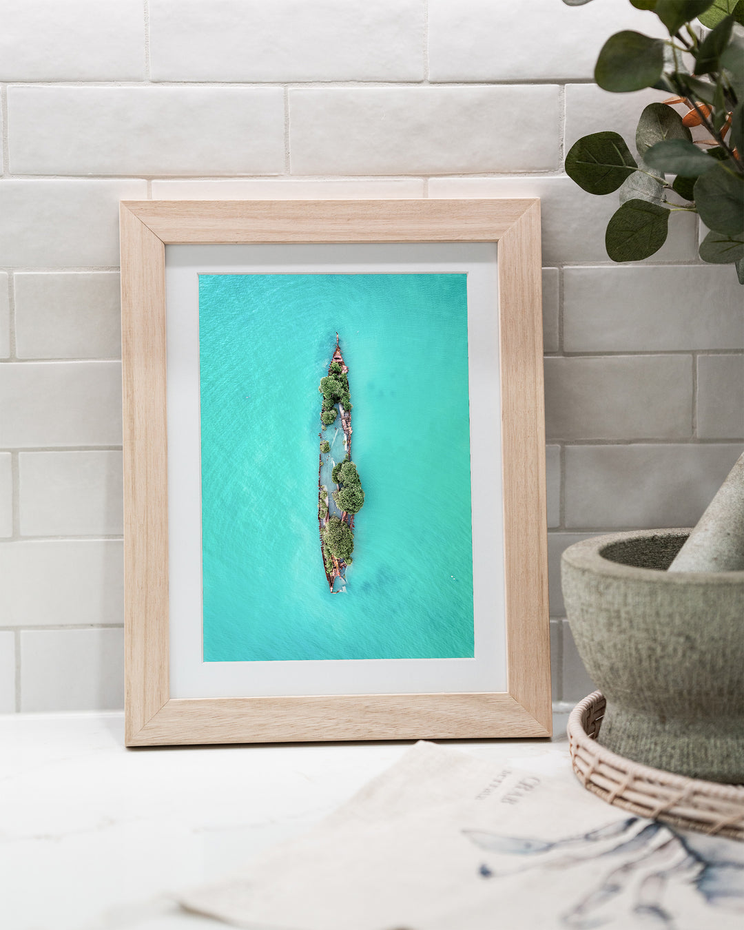 Sunken Solitude – Magnetic Island Shipwreck, Aerial Photography by David Lloyd, framed paper print in oak frame, styled in a kitchen bench setting