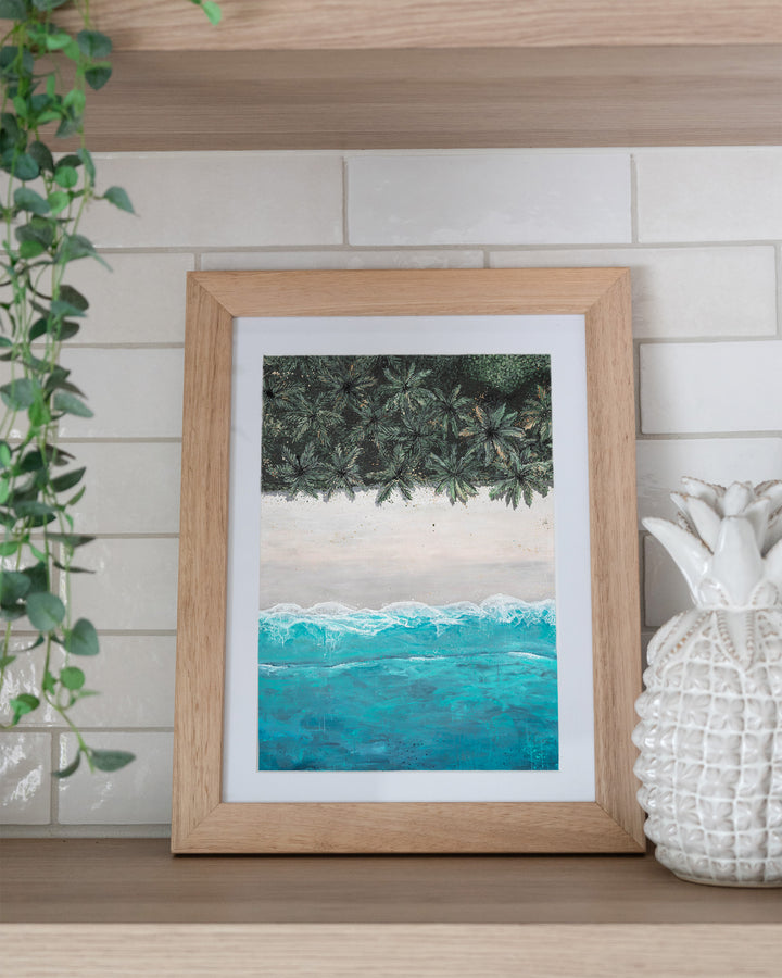 The Path Between – aerial beach and palm landscape, framed paper print in oak frame, styled on a kitchen shelf