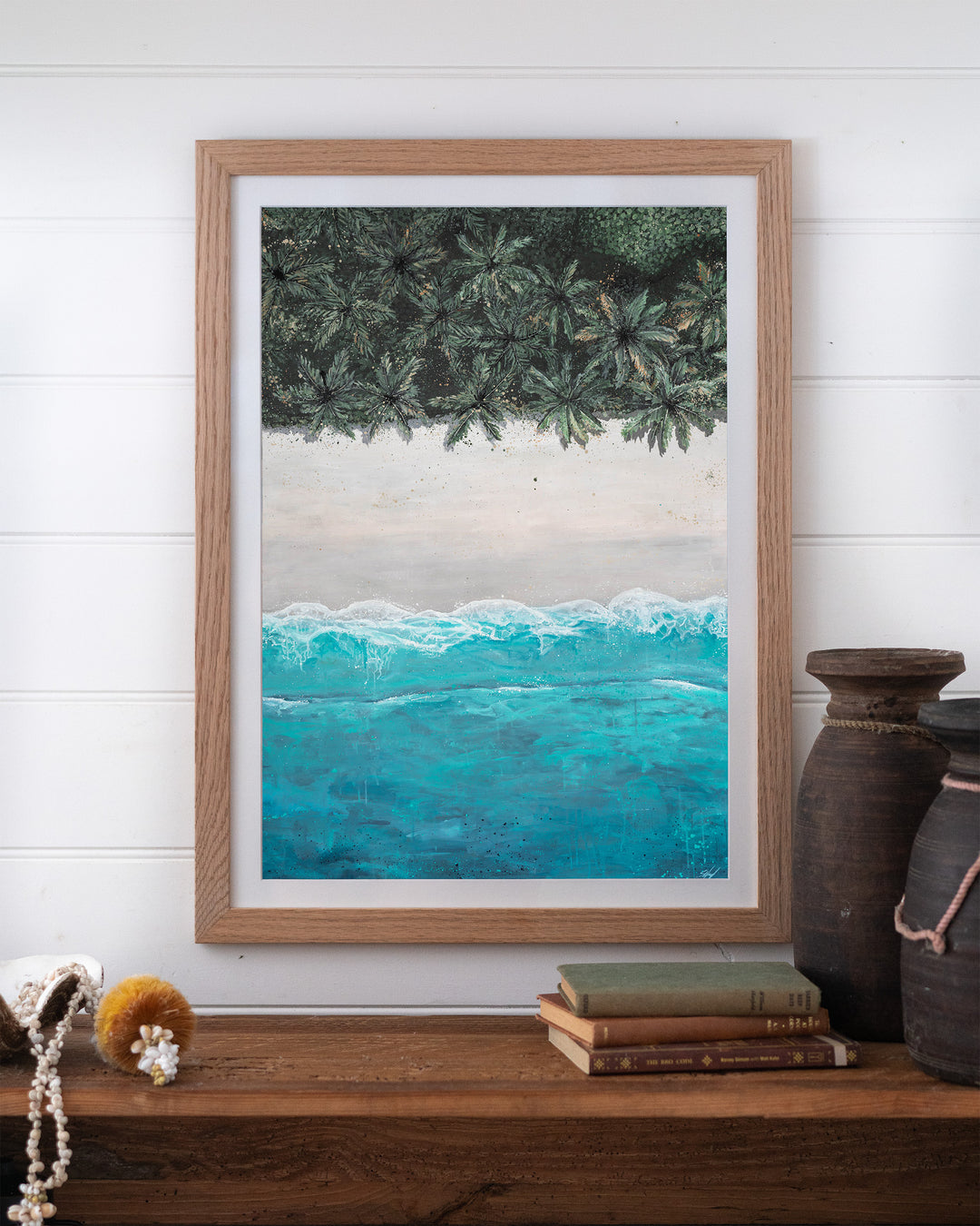 The Path Between – aerial beach and palm landscape, framed paper print in oak frame, styled on a timber shelf