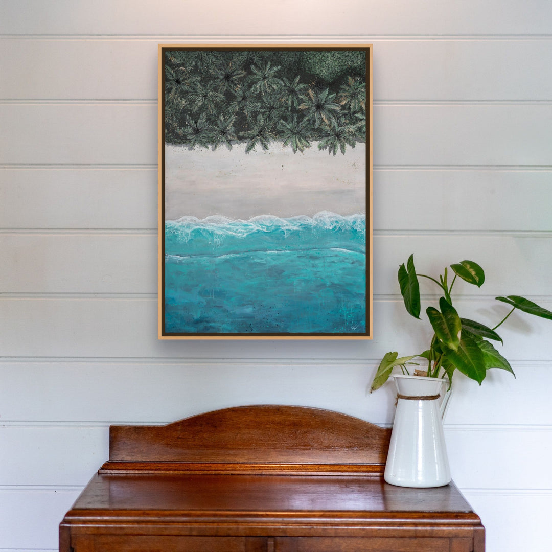 The Path Between artwork hangs above a wooden desk with a leafy plant in a white pitcher.
