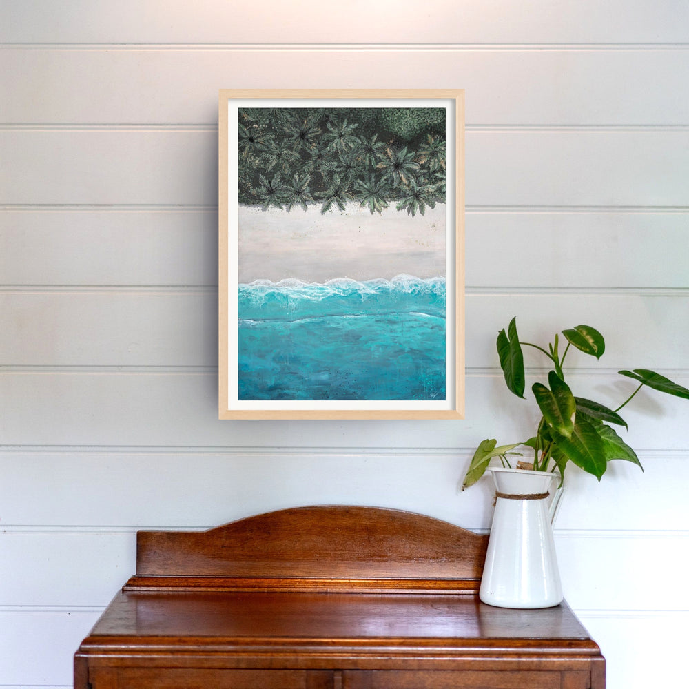 The Path Between print hangs above a wooden table topped with a leafy plant in a white vase.