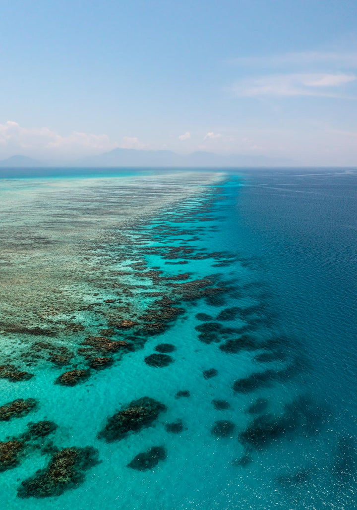 Tip of the Tongue – Aerial view of Tongue Reef with vibrant blue waters, coral bommies, and horizon blending into the mountains | Unframed Rolled Print