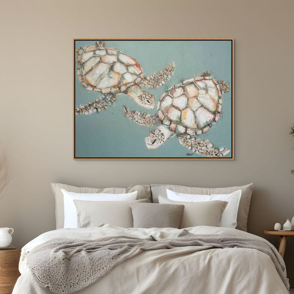 Framed artwork of two Turtle on a wall above a bed with neutral bedding.