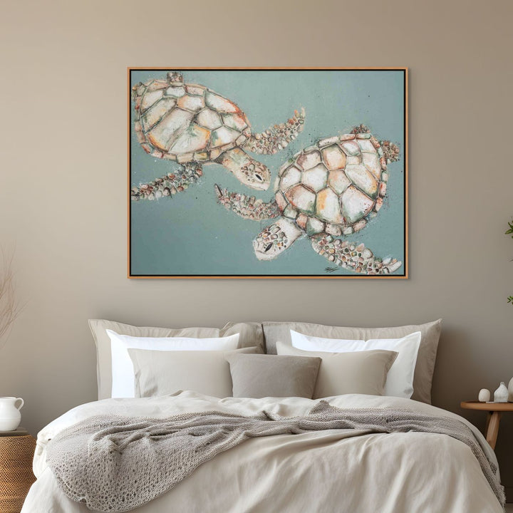 Framed artwork of two Turtle on a wall above a bed with neutral bedding.