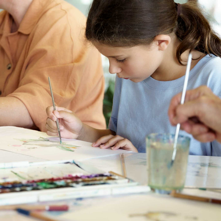 Two children painting with brushes at a table.