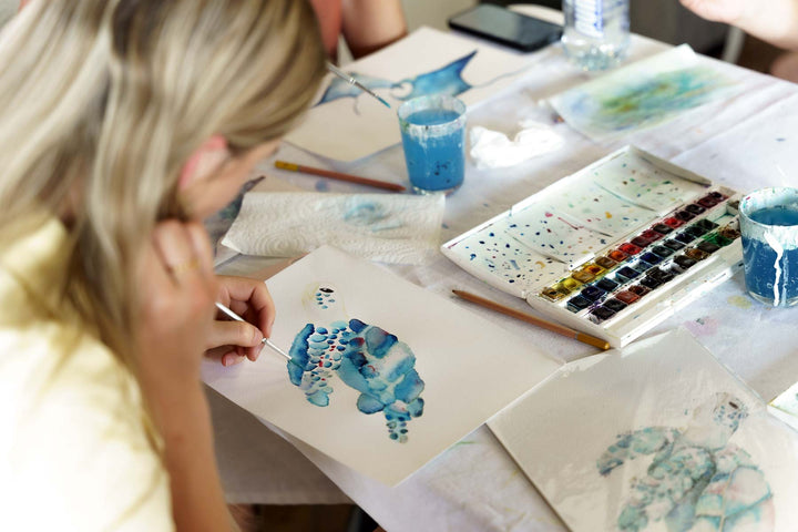 Person painting with watercolors at a table with art supplies