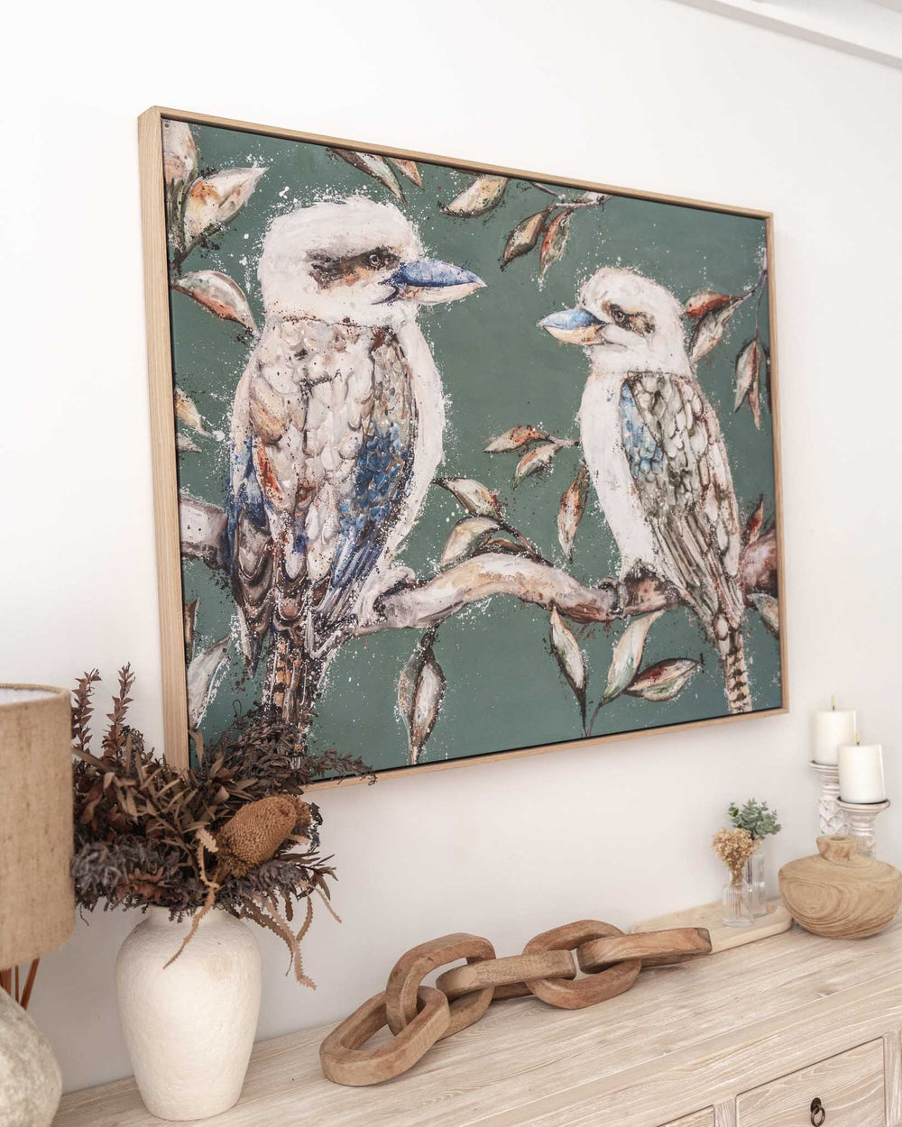 We Belong Together“ Kookaburras print hangs above a mantel decorated with vases, candles, and stacked wood.